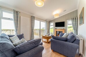 A cozy living room with two grey sofas, a wooden coffee table, a flat-screen TV, and a fireplace. - 2 Bed in Glenluce (oc-c36927) (Glenluce)