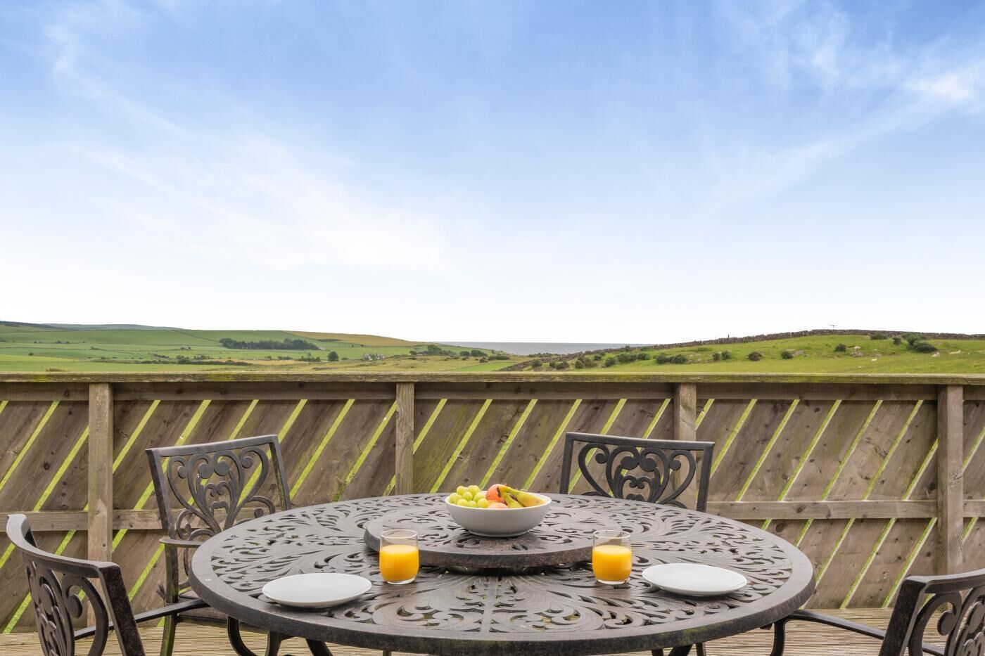 An outdoor dining area with a table and chairs, a bowl of fruit, and two glasses of orange juice.