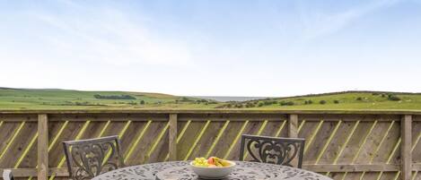 An outdoor dining area with a table and chairs, a bowl of fruit, and two glasses of orange juice.