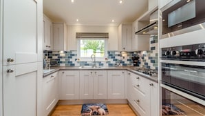 Uma cozinha moderna com armários brancos, painel de azulejos, uma janela e forno embutido.