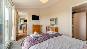 Quarto com cama, penteadeira, televisão e porta de vidro deslizante que dá para uma varanda.