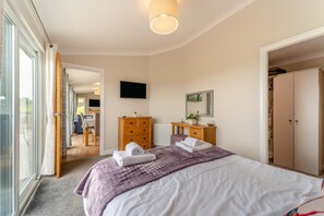 A bedroom with a bed, a dresser, a television, and a sliding glass door leading to a balcony. - 2 Bed in Glenluce (oc-c36927) (Glenluce)