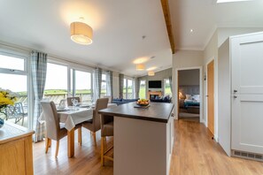 A modern kitchen with a dining area, large windows, and a view of the outdoors. - 2 Bed in Glenluce (oc-c36927) (Glenluce)