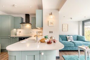 A modern kitchen with a central island, light blue cabinets, and a teal sofa in the living area. - 2 Bed in Tenby (oc-b41400) (Tenby)