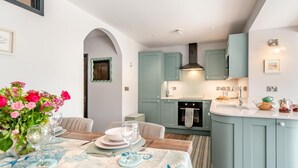 A modern kitchen with teal cabinetry, a central island, and a dining area with a table set for two. - 2 Bed in Tenby (oc-b41400) (Tenby)