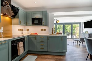 A modern kitchen with teal cabinetry, a central island, and a dining area with a view. - 2 Bed in Tenby (oc-b41402) (Tenby)