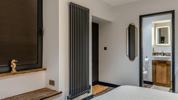 A hotel room with a bed, a radiator, a wooden shelf, a mirror, and a view into the bathroom. - 2 Bed in Tenby (oc-b41402) (Tenby)