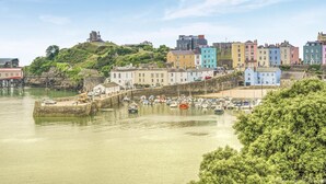 A coastal town with colorful buildings, a harbor with boats, and a hill with a structure on top. - 2 Bed in Tenby (oc-b41402) (Tenby)