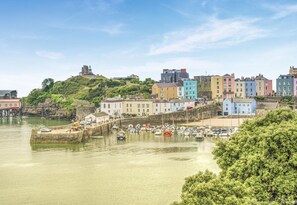 Uma cidade costeira com edifícios coloridos, um porto com barcos e uma colina com uma construção no topo.