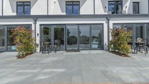 A modern building with a glass entrance, outdoor seating area, and a paved patio. - 2 Bed in Tenby (oc-b41402) (Tenby)