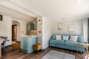 Uma sala de estar moderna com um sofá azul, um banquinho de madeira e uma área de jantar com mesa e cadeiras.