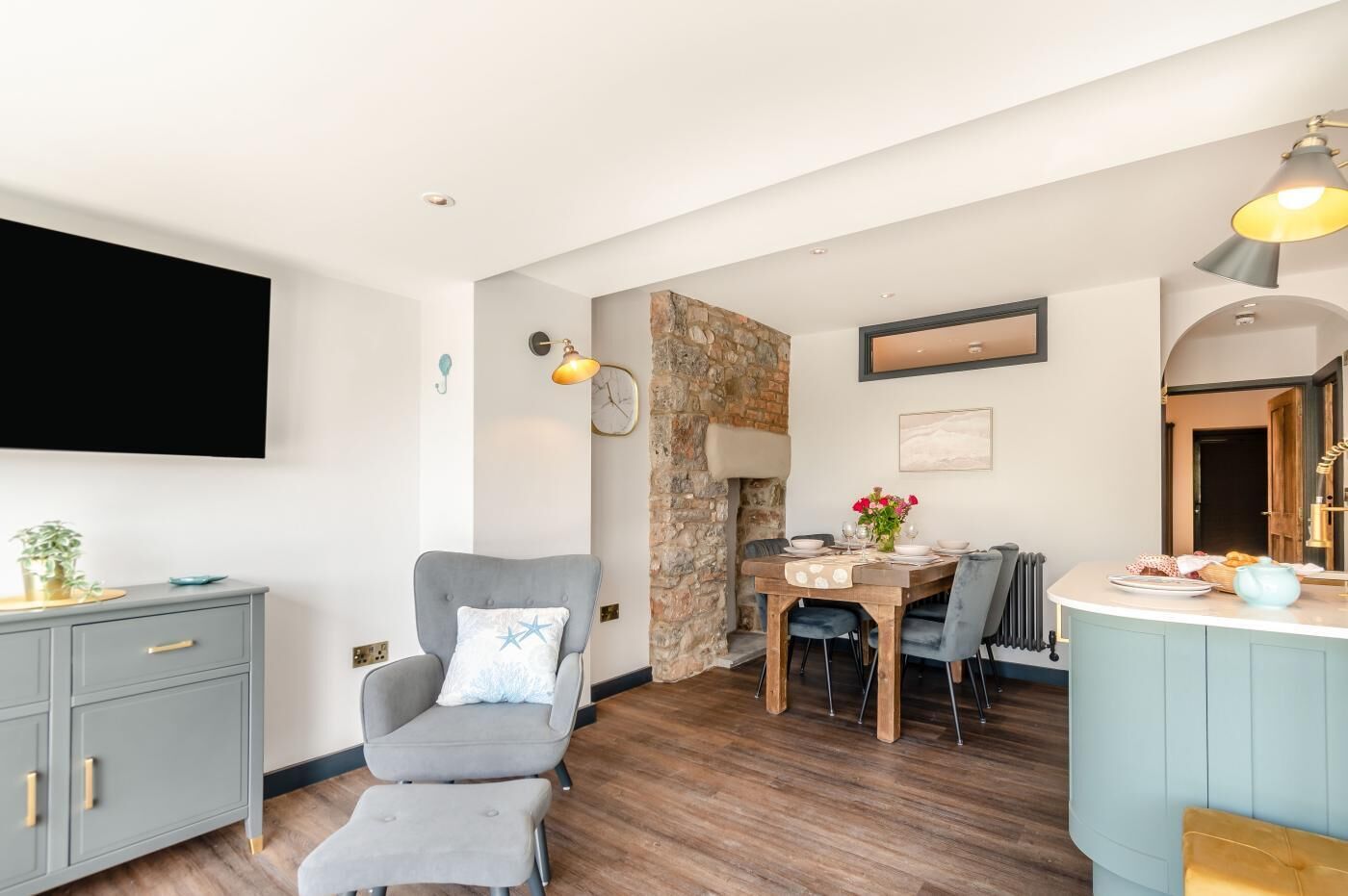 Un salon moderne avec un canapé gris, une table à manger avec des chaises et un coin cuisine doté d’un plan de travail bleu.