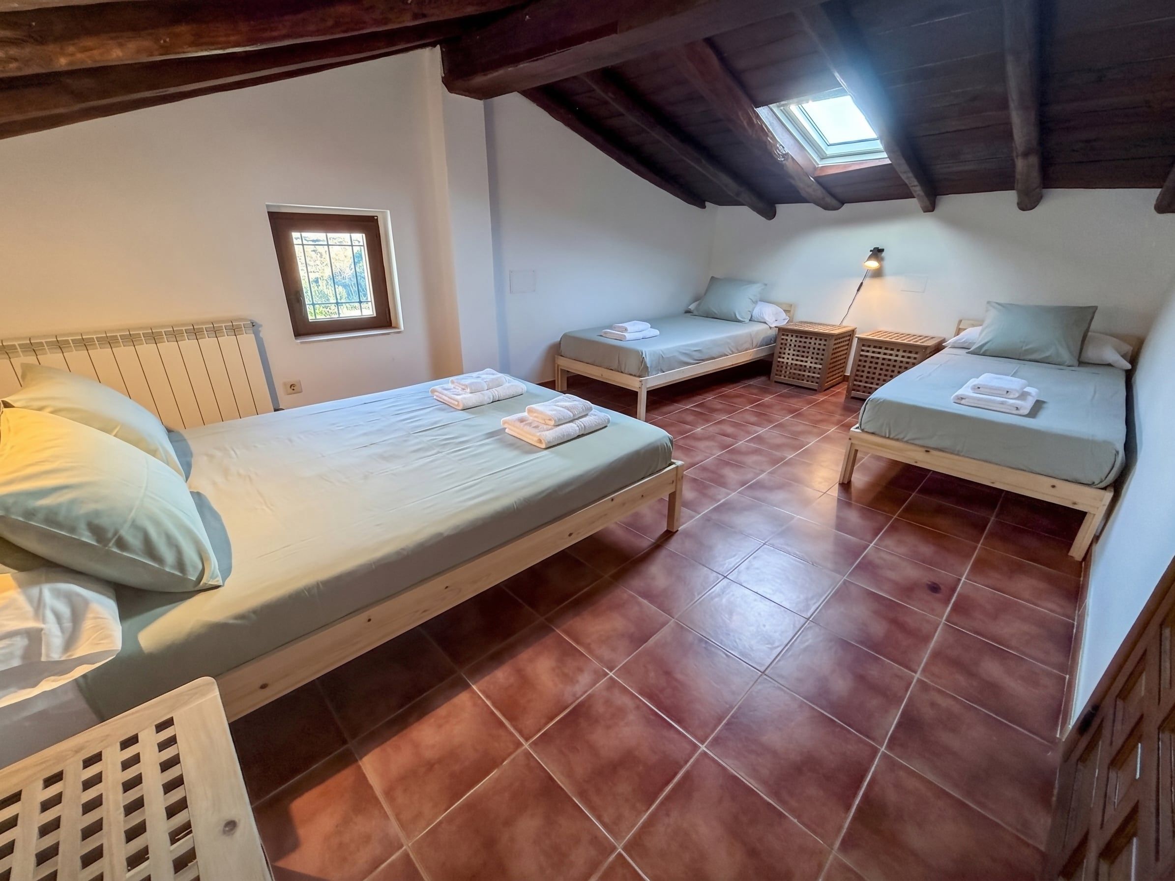 A small, cozy room with two beds, a window, and a skylight.