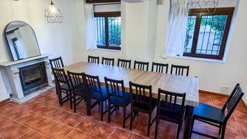 A dining area with a long wooden table, chairs, a fireplace, and windows with curtains.