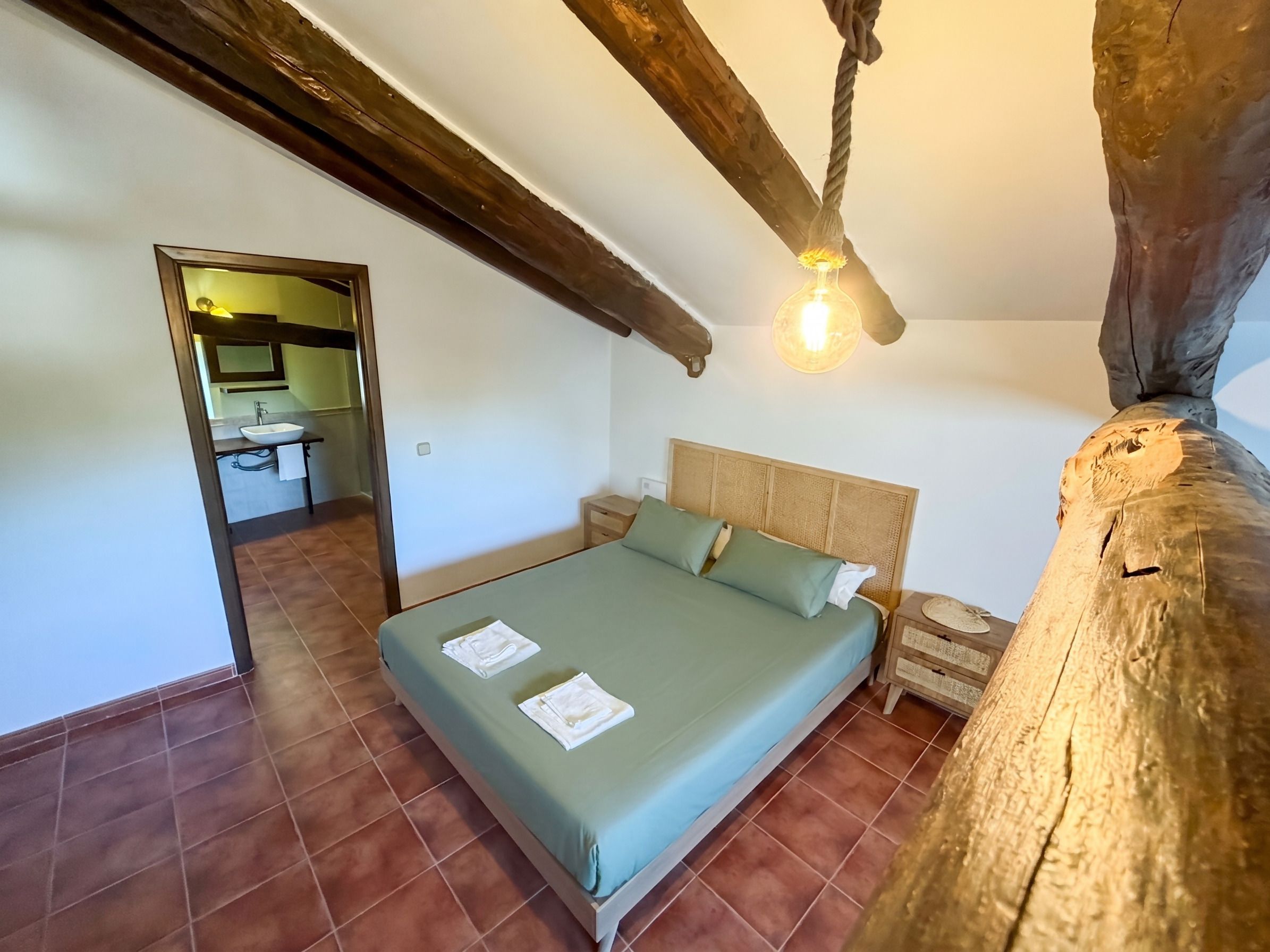 A bedroom with a bed, a nightstand, a mirror, and a wooden beam ceiling.