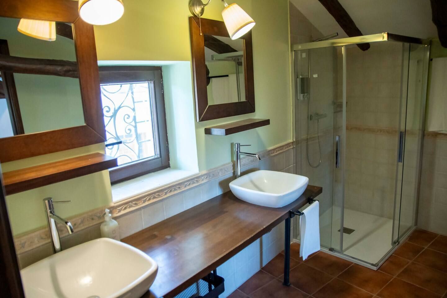 A bathroom with two sinks, a shower, and a window with a decorative iron grille.