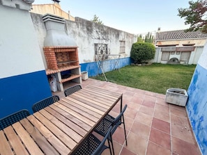 Eine Terrasse im Freien mit einem Grill aus Ziegelsteinen, einem Holztisch und Stühlen.