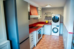 Eine kompakte Küche mit roter Arbeitsplatte, einem eingebauten Backofen, einer Waschmaschine und einem kleinen Spülbecken.