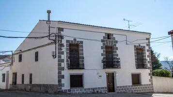 A two-story building with a white facade and stone accents, featuring two balconies with metal railings.