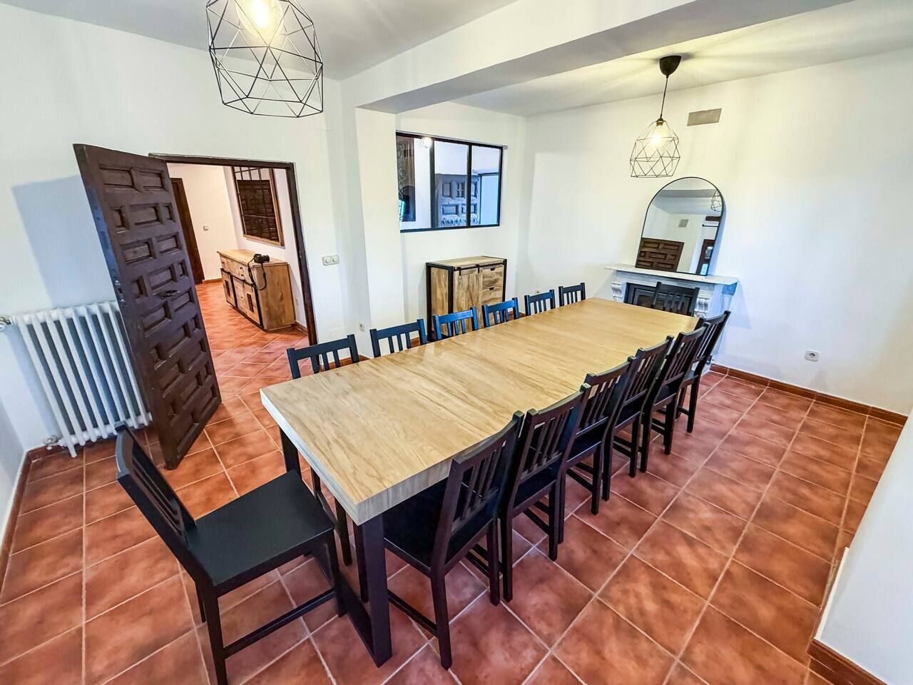 A dining room with a large wooden table and chairs, a radiator, and a window with a view.