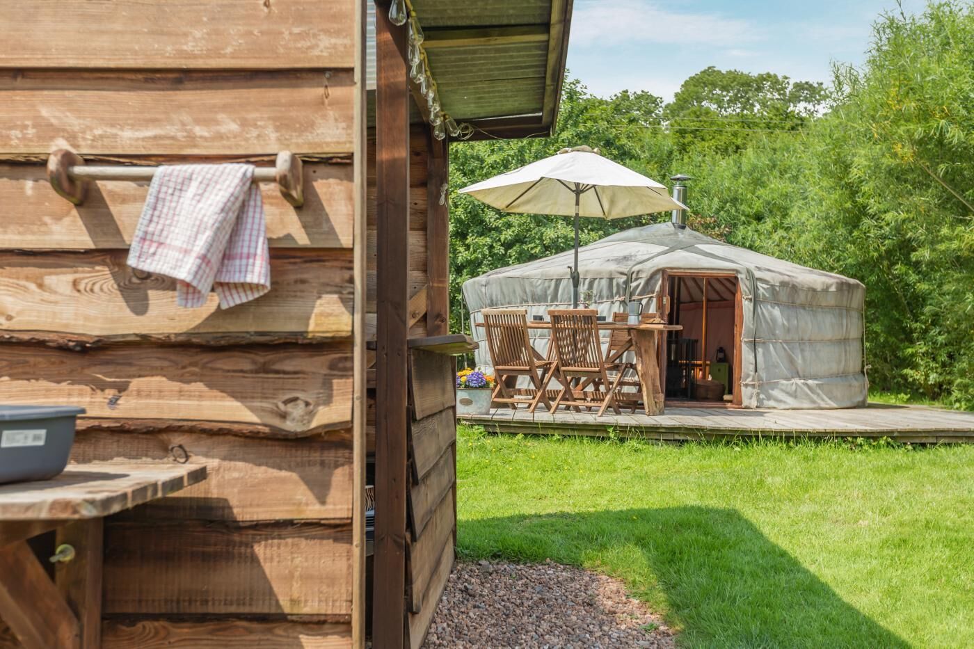 Een houten blokhut met een overdekt terras en een tentachtige constructie.