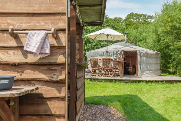 A wooden cabin with a covered outdoor seating area and a tent-like structure.