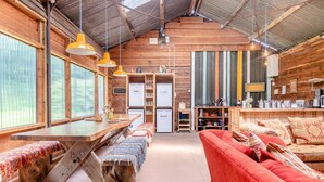 Interior rústico de una cabaña con una mesa de comedor de madera, bancos, un sofá y una zona de cocina.