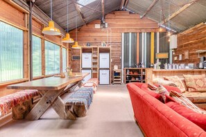 A rustic cabin interior with a wooden dining table, benches, a sofa, and a kitchen area. - 1 Bed in Blackborough (oc-w42630) (Blackborough)
