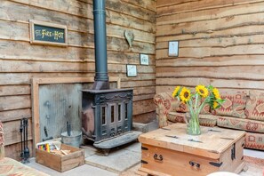 A rustic cabin interior with a wood-burning stove, a sofa with patterned cushions, and a vase with sunflowers on a wooden table. - 1 Bed in Blackborough (oc-w42630) (Blackborough)