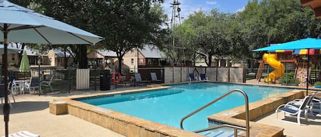 Una piscina con un puesto de salvavidas, sillas de descanso y un molino de viento al fondo.