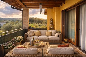 A balcony with a wicker sofa, a table with a bottle and glasses, and a view of the countryside. - Sunshine Luxury Apartment: Lake View, Patio, Pool, Spacious House (Padenghe Sul Garda)