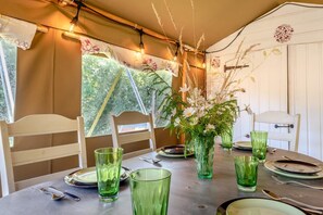 Ett matbord dukat med grönt glas, tallrikar och bestick, med en blomsterdekoration i mitten och ljusslingor.