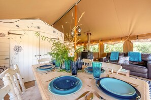 A tented accommodation with a dining table set for four, surrounded by chairs.