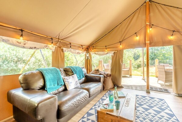 A tented accommodation with a leather sofa, a coffee table, and string lights.