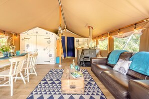 Eine Zelthotelunterkunft mit Essbereich, Küchenzeile und Wohnbereich inklusive Sofa und Couchtisch.