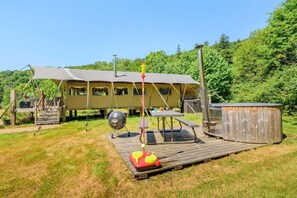 Un camping con terraza de madera, una parrilla, un jacuzzi y una estructura cubierta.