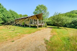 A modern, open-air structure with a sloped roof, surrounded by a grassy area and trees. - 3 Bed in Newcastle Emlyn (oc-t42686) (Cwm-cou)
