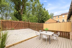 Eine Holzterrasse mit Tisch und Stühlen, umgeben von einem Holzzaun und Bäumen.