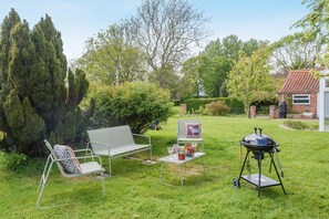 Ein Garten mit Grill, einer Bank, einem Stuhl und einem Tisch mit Getränken und Obst.