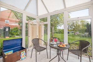 A conservatory with wicker chairs, a table with breakfast items, and a blue chest of drawers. - 3 Bed in Sloothby (oc-i42705) (Sloothby)