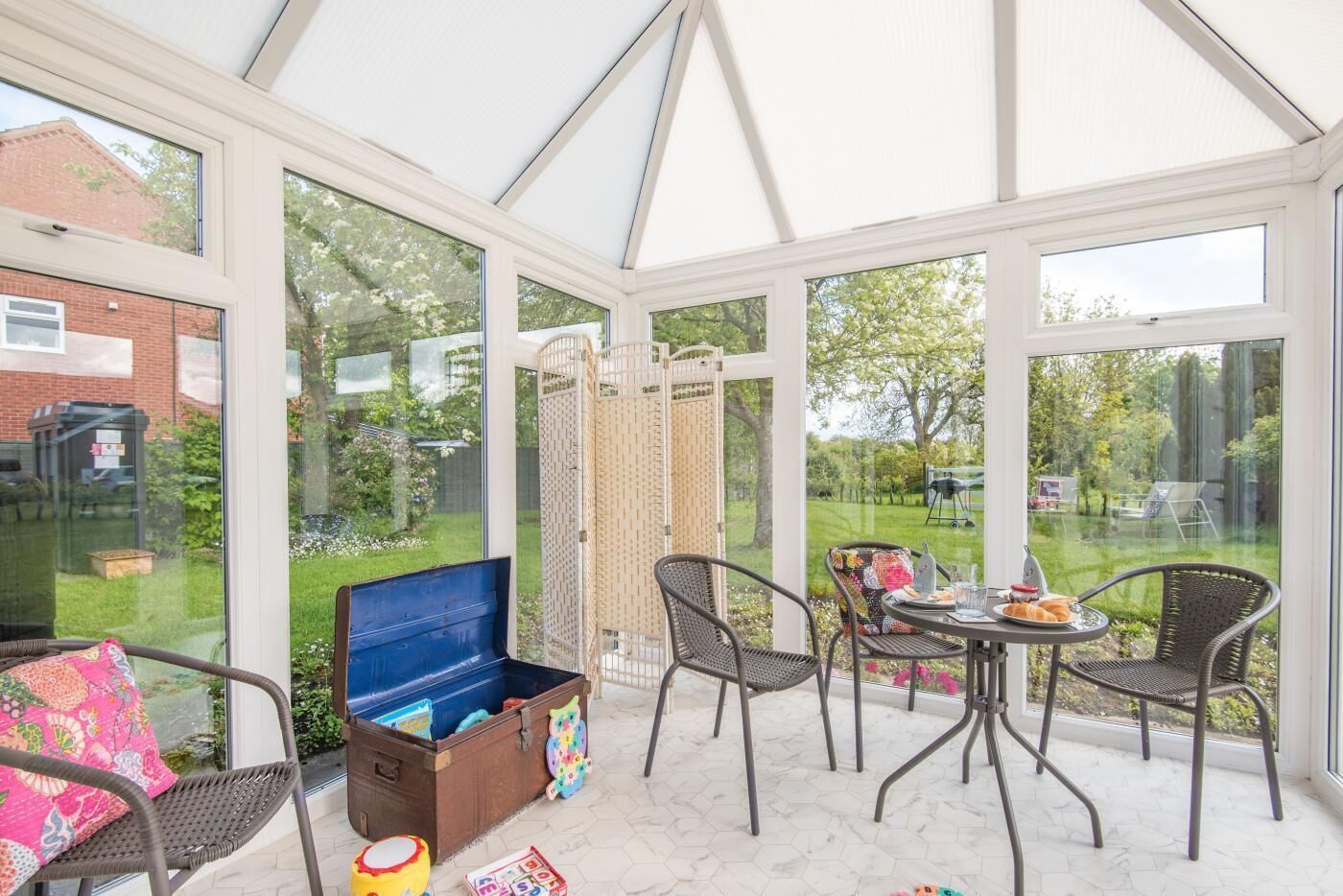 Een oranjerie met een tafel, stoelen, een blauwe kledingkast en uitzicht op een tuin.