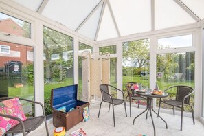 A conservatory with a table and chairs, a blue chest of drawers, and a view of a garden. - 3 Bed in Sloothby (oc-i42705) (Sloothby)