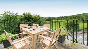Een terras met een tafel en stoelen, omgeven door een zwarte metalen hek, met uitzicht op een weelderig groen landschap.
