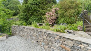 Een stenen keerwand met een grindpad, omringd door weelderige begroeiing en bloeiende planten.