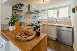 A modern kitchen with wooden countertops, a built-in oven, a dishwasher, and a window providing natural light. - 3 Bed in St. Ives (oc-d42669) (St Ives)