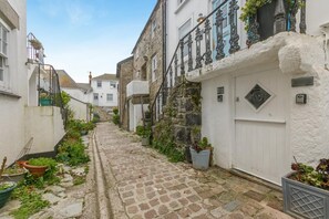 A narrow cobblestone street flanked by buildings with white walls and black iron railings. - 3 Bed in St. Ives (oc-d42669) (St Ives)