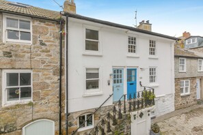 A two-story white building with a blue door, stone walls, and a small balcony with a wrought iron railing. - 3 Bed in St. Ives (oc-d42669) (St Ives)