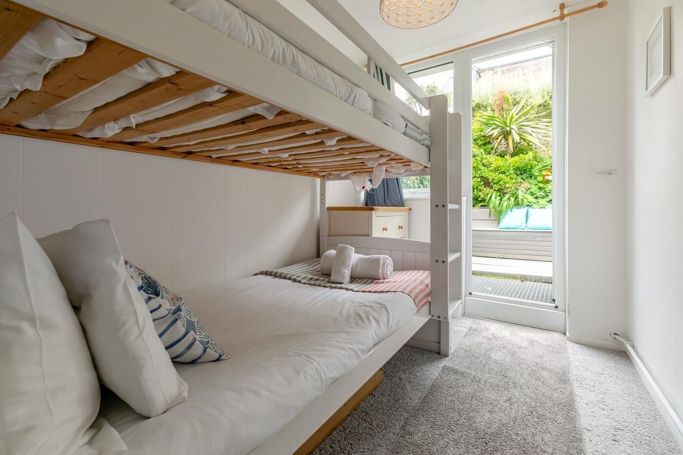A bunk bed room with a view of a garden through an open door.