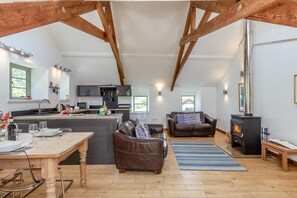 A spacious loft with exposed wooden beams, a kitchen with modern appliances, a cozy seating area with a fireplace, and a dining table set for two. - 2 Bed in Cotmore (oc-a44749) (Beeson)