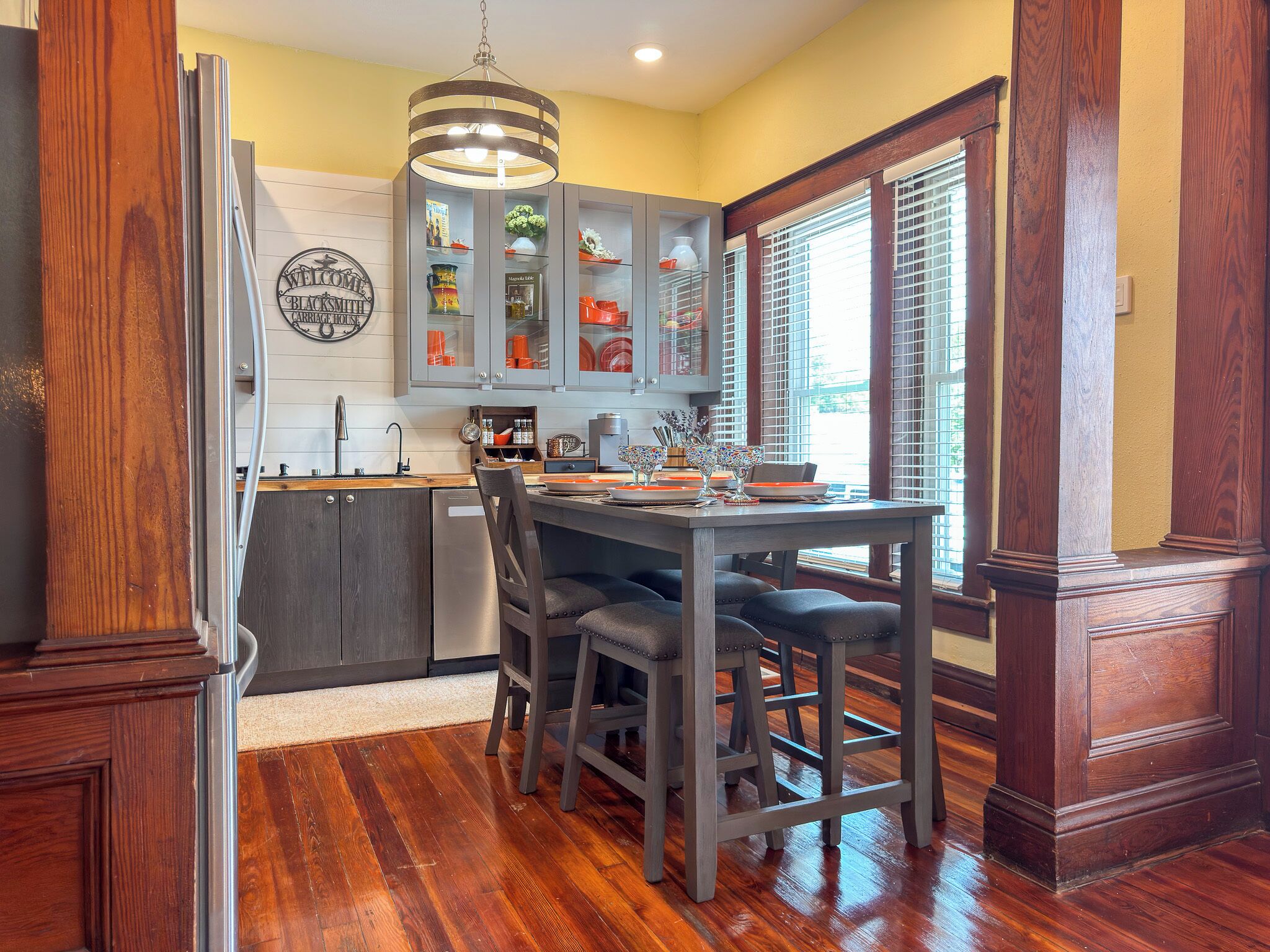 Una cocina con una mesa y sillas de madera, una lámpara colgante y una ventana con persianas.